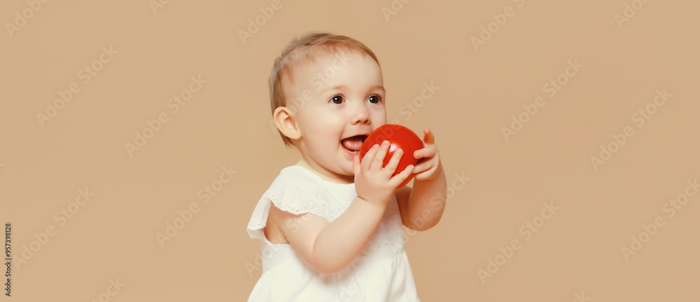 Cute baby holding red apple fruit sitting on the floor on brown studio background Cute baby holding red apple fruit sitting on the floor on brown studio background