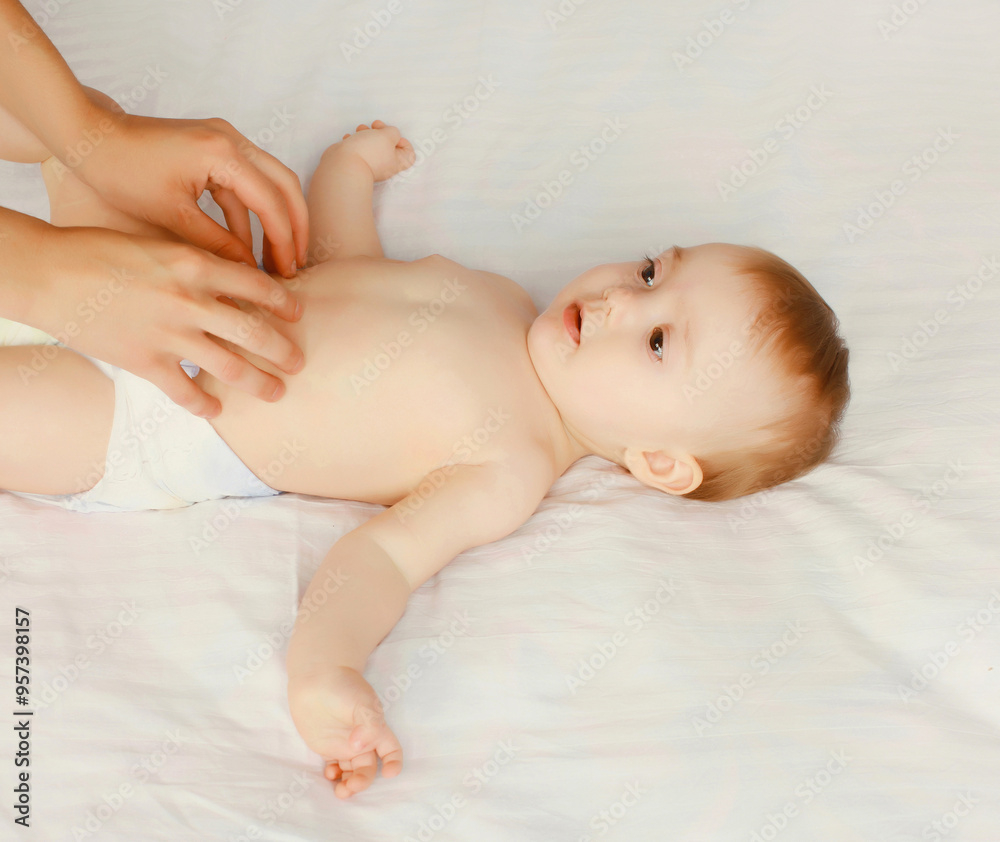 mother gives massage to baby lying on the bed on white background mother gives massage to baby lying on the bed on white background