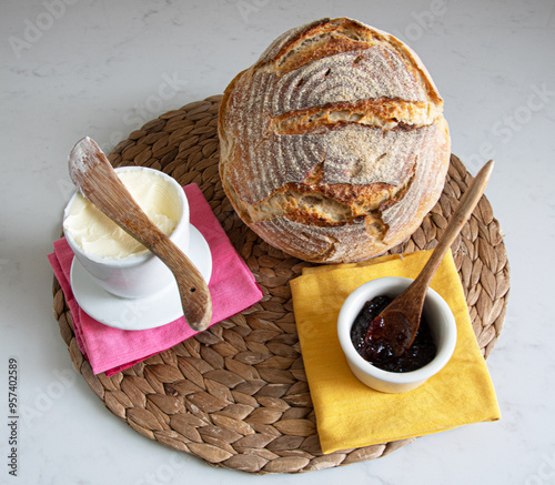A round load of homemade sourdough bread pictured with butter and a container of jam on pink and yellow napkins.