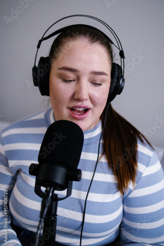 Close-up of female podcaster in headphones speaking into microphone 