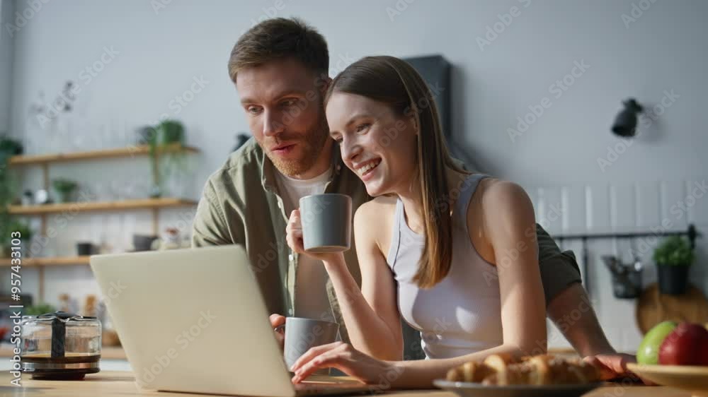 Talking couple browsing laptop website drinking coffee in kitchen closeup. 