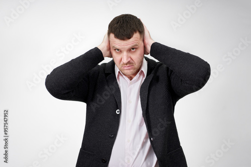 Young businessman closing ears with hands on grey background