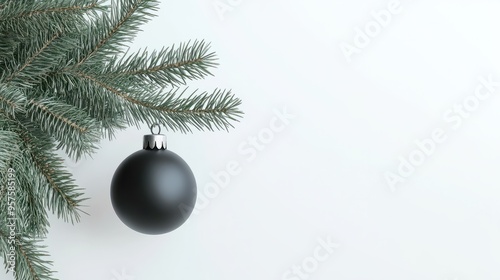 Minimalistic christmas concept featuring a single black bauble hanging on a natural fir tree branch against a clean white background