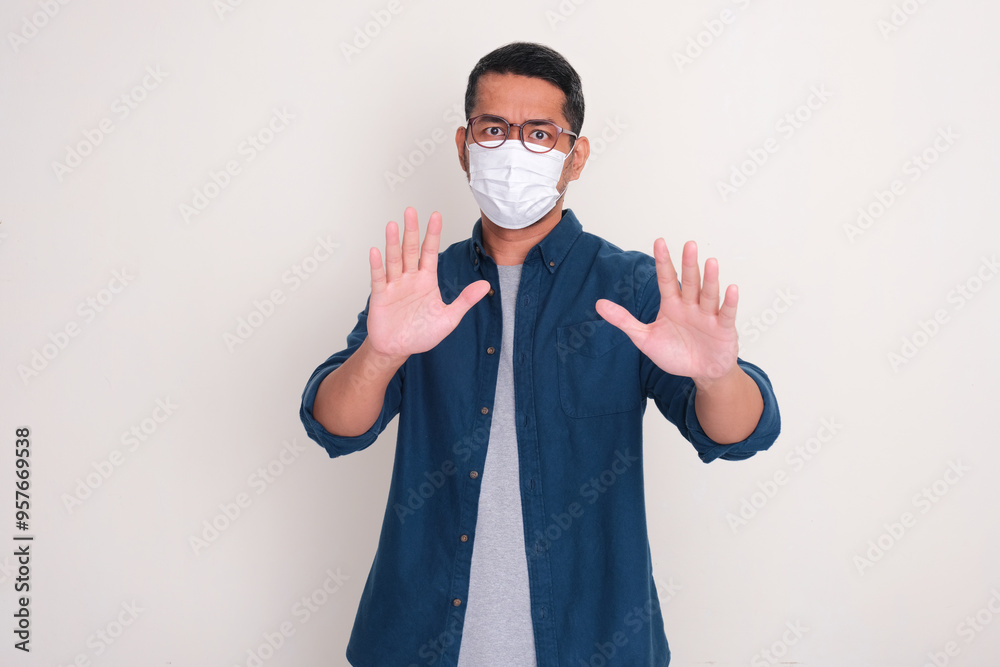 A man wearing medical face mask doing stop hand sign with serious expression