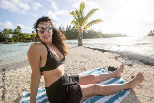 Beautiful middle aged woman sitting on a sandy beach on a tiny private island or motu in French Polynesia.