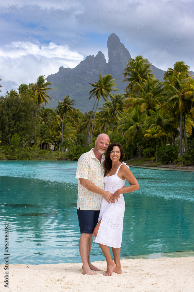 Happy, middle aged couple together on vacation on tropical island Bora Bora. Palm trees, an azure ocean lagoon and Mount Otemanu can be seen in the background.