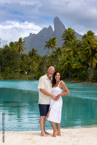 Obraz na płótnie Happy, middle aged couple together on vacation on tropical island Bora Bora. Palm trees, an azure ocean lagoon and Mount Otemanu can be seen in the background. w salonie