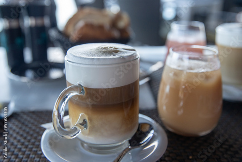 Fresh hot cappuccino coffee with a frothy top. The caffeine drink is served in a glass mug in a cafe or diner. Another popular option is a latte. 