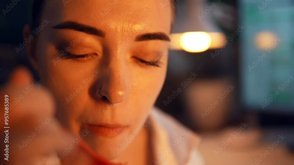 Portrait of Caucasian woman eating instant noodles and drinking its bouillon from plastic container in the late evening at work. Tired female employee is having fast ramen soup for lunch at the job