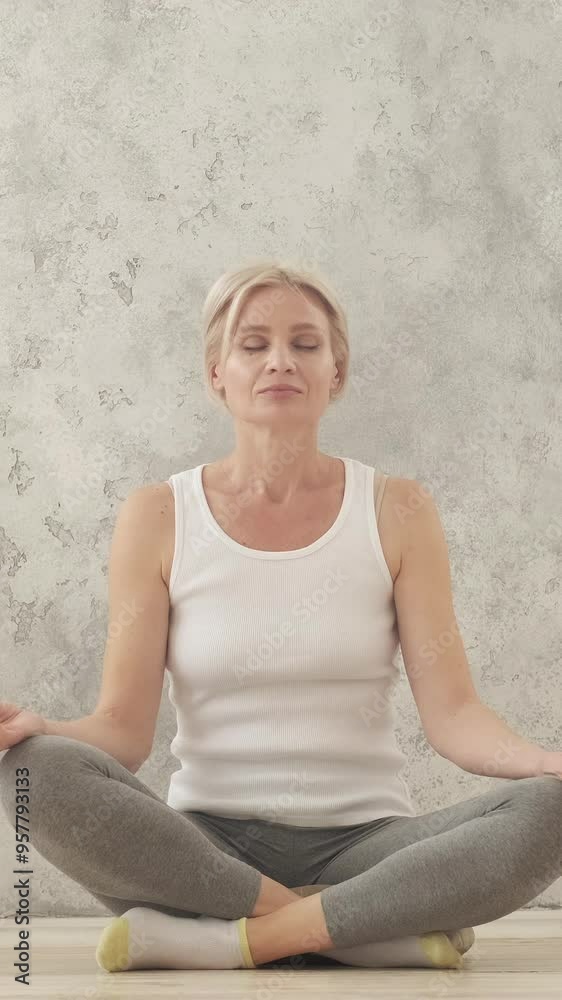 Vertical video. Peaceful mind. Domestic meditation. Home practice. Relaxed happy smiling woman in sportswear sitting in lotus pose on floor in light interior. Vertical video. Peaceful mind. Domestic meditation. Home practice. Relaxed happy smiling woman in sportswear sitting in lotus pose on floor in light interior.