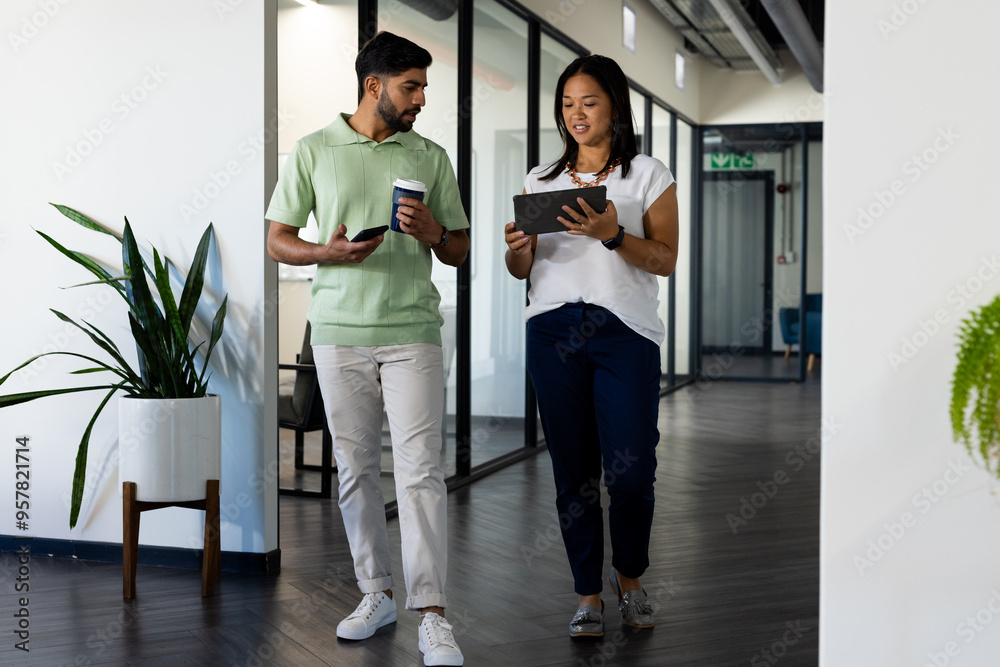 Walking in office, colleagues discussing project while holding tablet and coffee cup
