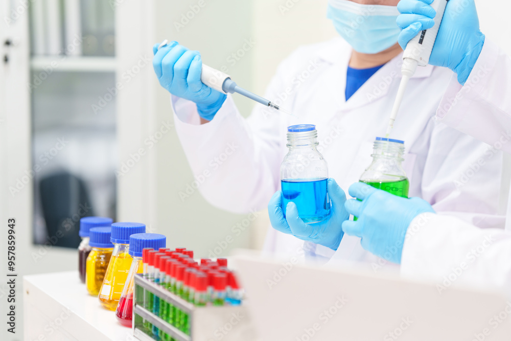 Two Asian scientists in lab coats sit at a table in a laboratory, examining samples through a microscope. The room is equipped with scientific tools, liquids, and chemistry materials. Two Asian scientists in lab coats sit at a table in a laboratory, examining samples through a microscope. The room is equipped with scientific tools, liquids, and chemistry materials.