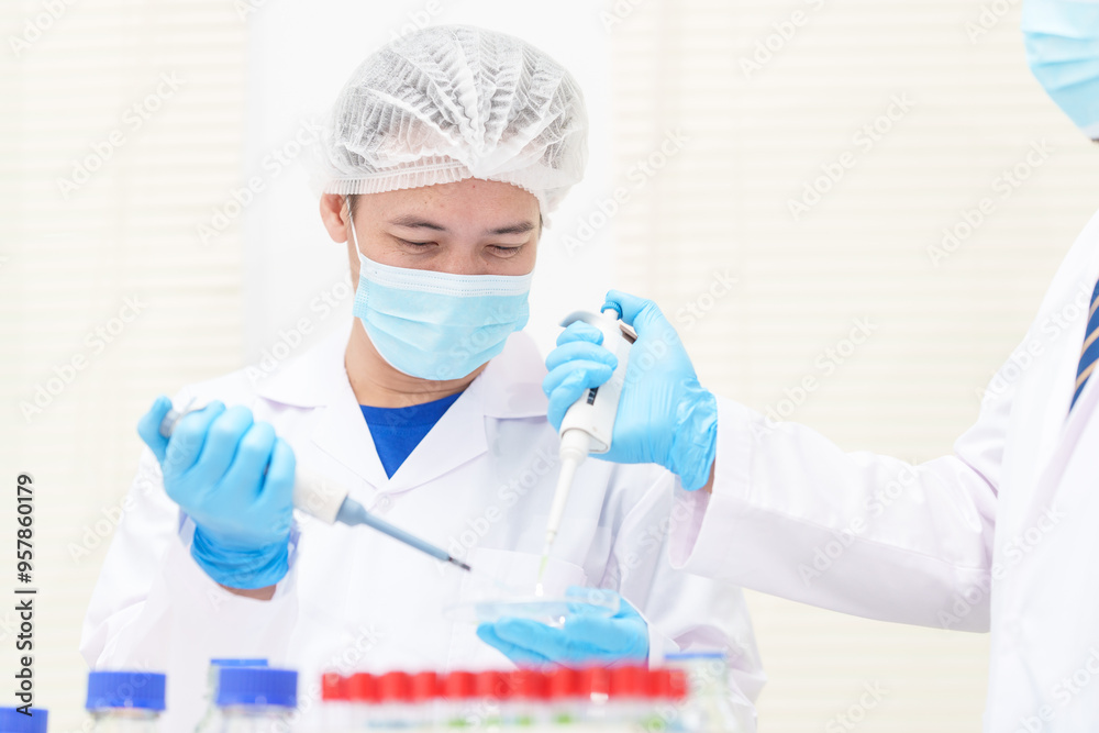 Two Asian scientists in lab coats sit at a table in a laboratory, examining samples through a microscope. The room is equipped with scientific tools, liquids, and chemistry materials. Two Asian scientists in lab coats sit at a table in a laboratory, examining samples through a microscope. The room is equipped with scientific tools, liquids, and chemistry materials.
