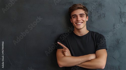 Young man isolated on gray textured wall, smiling while pointing with index finger to black t-shirt, copyspace for advertising