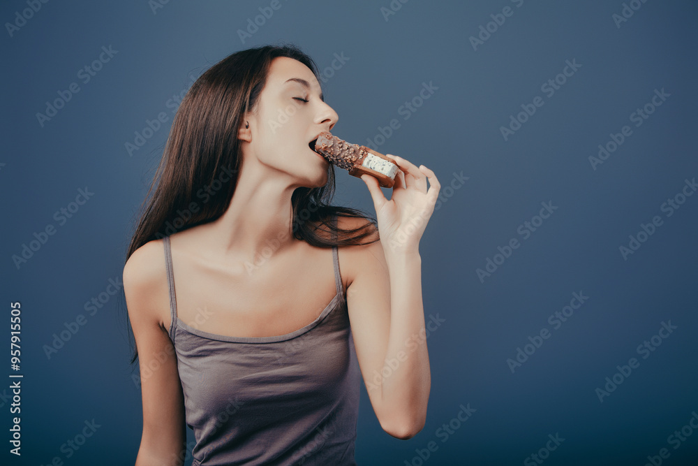 Young woman enjoying eating ice cream bar on blue background Young woman enjoying eating ice cream bar on blue background
