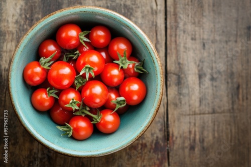 A top-down view of a bowl filled with small, red tomatoes, placed on a wooden surface.