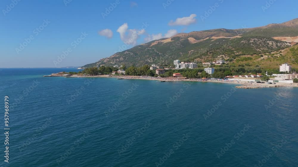 Coastal town nestled between blue sea and green mountains under a bright, clear sky Coastal town nestled between blue sea and green mountains under a bright, clear sky