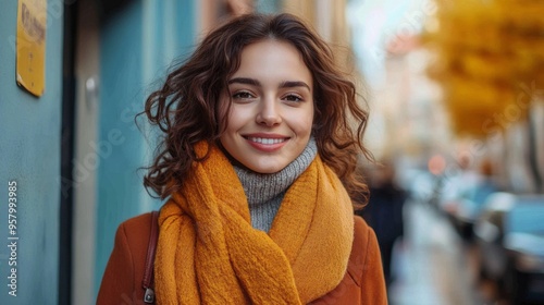 A woman wearing a yellow scarf and a brown coat is smiling