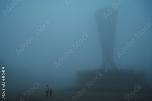 backs of mother woman with child son walking in a misty foggy mystical park in evening. A misty landscape with people in autumn in a misty fog mist haze in Independence Park in Shymkent in Kazakhstan photo