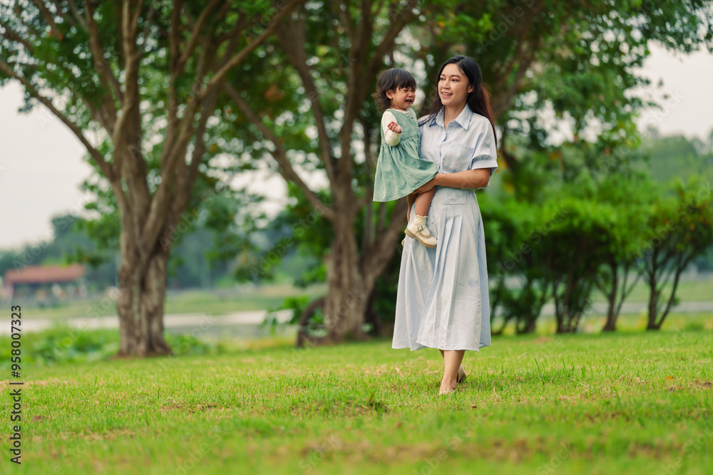 mother holding crying toddler baby girl while walking on grass field in park mother holding crying toddler baby girl while walking on grass field in park