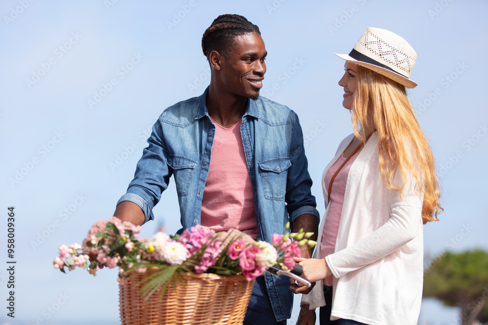 multiracial couple stood by bicycle with flowers in basket