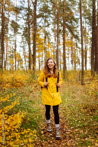 Young woman in a yellow raincoat exploring a vibrant autumn forest filled with colorful foliage during a sunny afternoon hike. Autumn landscape.