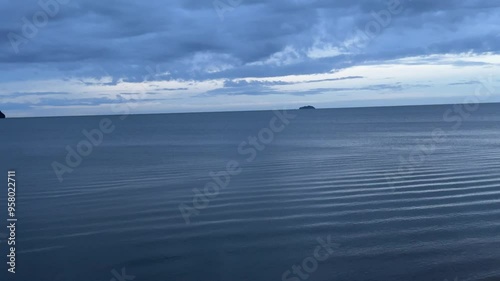 The deep blue sea has slight waves from the wind and deep blue clouds float above.