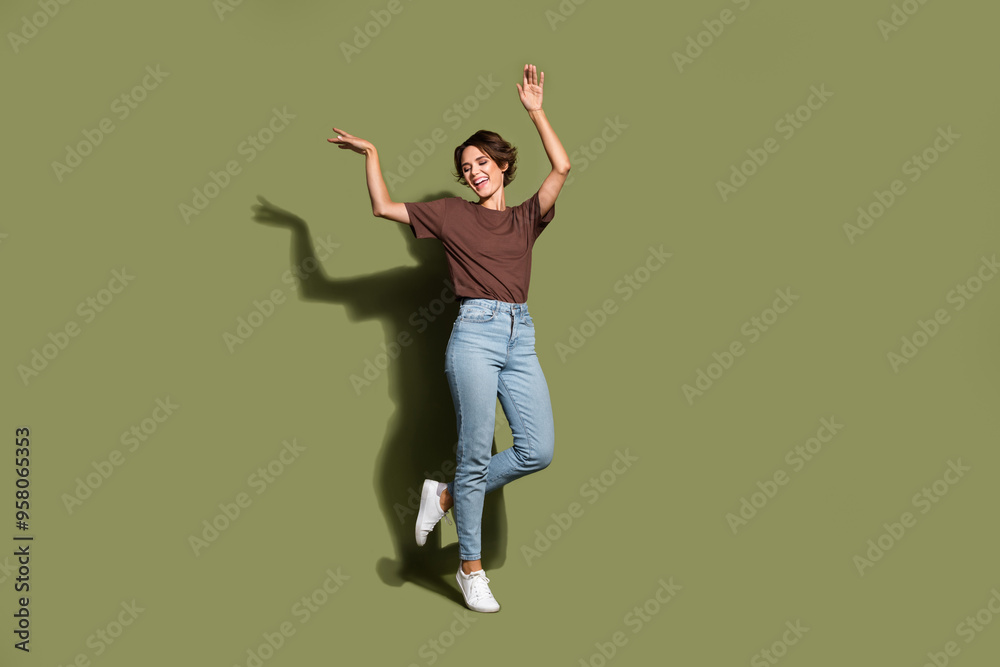 Full length photo of satisfied cheerful girl wear oversize t-shirt denim pants holding hands up isolated on green color background