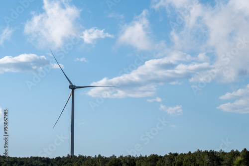 A single wind turbine stands tall under a blue sky with scattered clouds, showcasing renewable energy in harmony with the natural landscape in Tarragona Spain