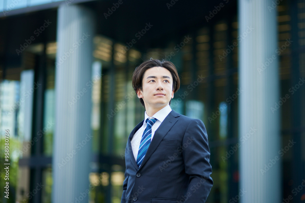 遠くを見つめるスーツを着た若いビジネスマンとオフィスビル 遠くを見つめるスーツを着た若いビジネスマンとオフィスビル