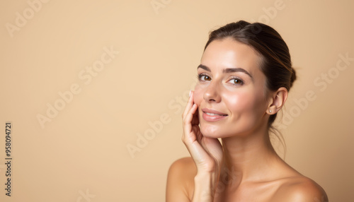 A close-up of a woman with radiant skin, smiling gently while touching her face against a soft beige background.