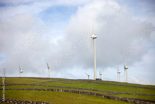 Wind turbines on rolling hills in Terceira Island, Azores, Portugal. The turbines stand tall against a clear sky, harnessing renewable energy amidst lush green landscapes. Serene and sustainable energ photo