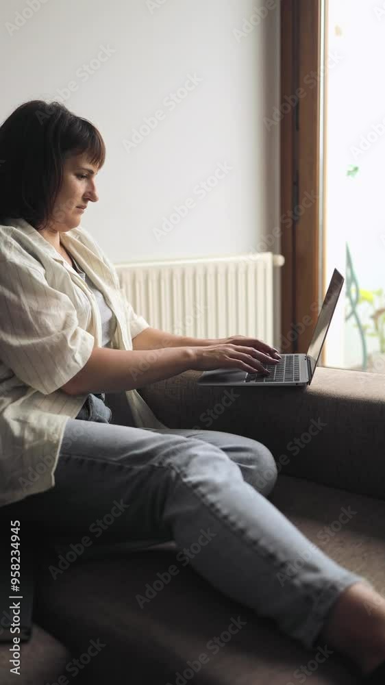 Vertical video of lady works remotely from a computer, laptop, remote work, online, work from home, technology, typing on a keyboard, searching in Internet, girl sitting on couch, comfort, freelancer Vertical video of lady works remotely from a computer, laptop, remote work, online, work from home, technology, typing on a keyboard, searching in Internet, girl sitting on couch, comfort, freelancer