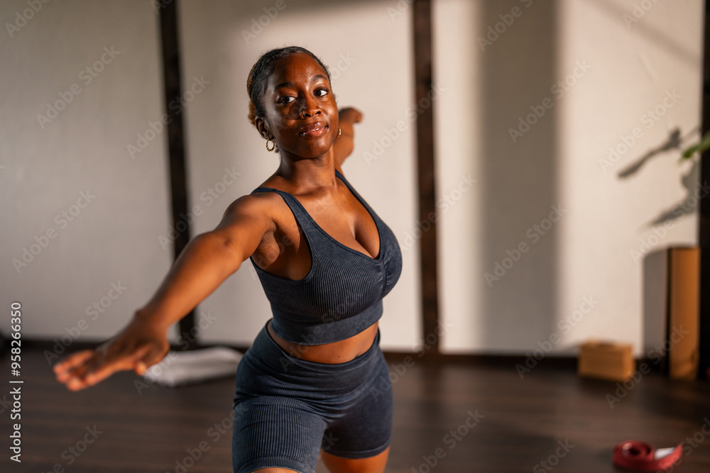Young woman practicing yoga in a studio, performing the Warrior II pose on a yoga mat. She is wearing a matching dark blue sports bra and shorts set. Young woman practicing yoga in a studio, performing the Warrior II pose on a yoga mat. She is wearing a matching dark blue sports bra and shorts set.