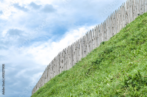 Old wooden fence with sharp endings on grass hill, Castle defensive wall, aged heritage architecture