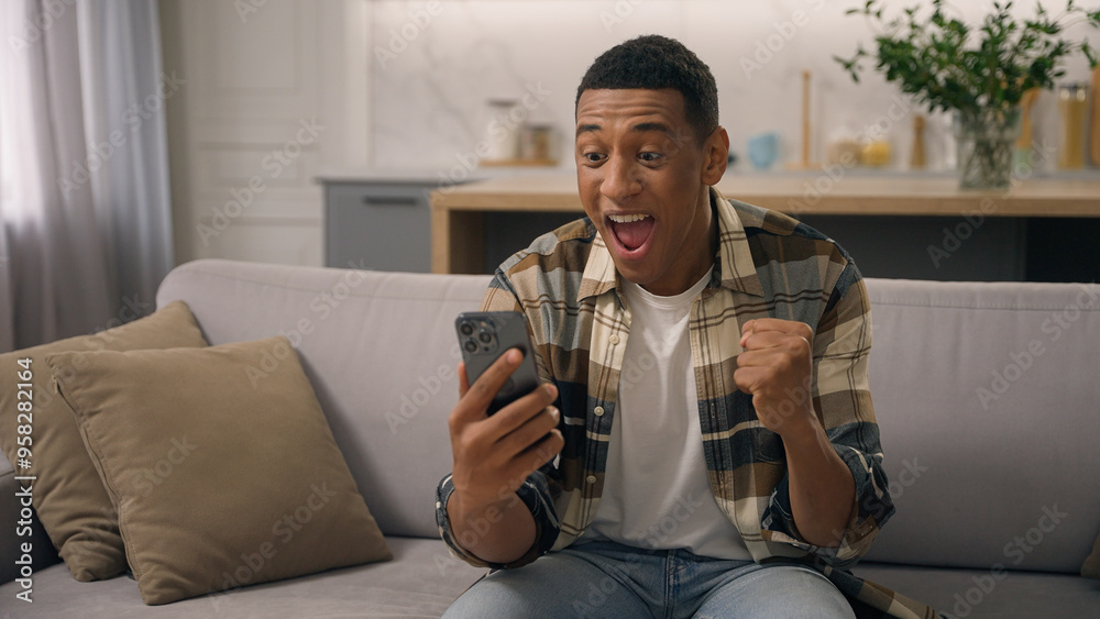 Wow African American man surprised wonder amazed win with phone mobile shocked sudden victory good winning news biracial male ethnic guy celebrating online success achieve offer excited on sofa couch Wow African American man surprised wonder amazed win with phone mobile shocked sudden victory good winning news biracial male ethnic guy celebrating online success achieve offer excited on sofa couch