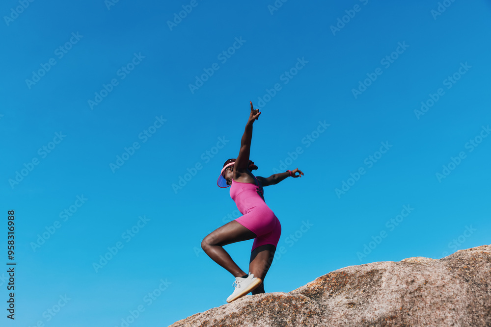 Woman in pink dress posing on a rock against a clear blue sky Woman in pink dress posing on a rock against a clear blue sky