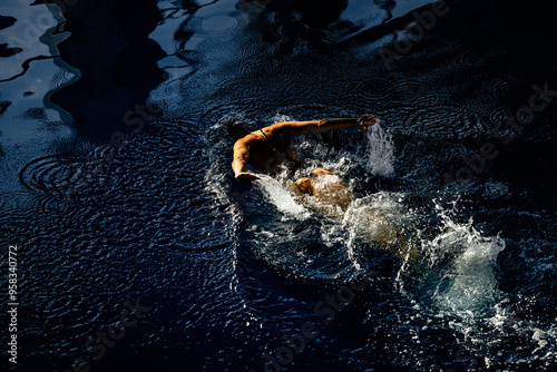 Female athlete swims with a butterfly style. Splashes of water scatter in different directions