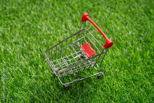 A miniature shopping cart on vibrant green grass with copy space symbolizes sustainable shopping. Eco-friendly consumerism, emphasizing environmental awareness and responsible purchasing concept. photo