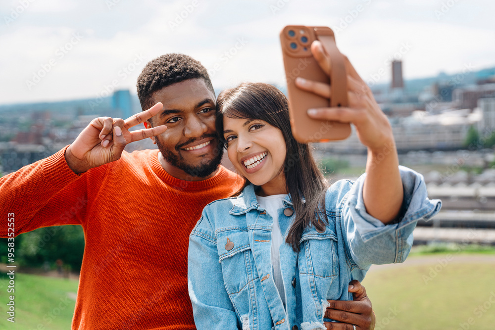 Naklejka premium A Joyful Couple Takes a Selfie on a Sunny Day in the City Park Surrounded by Greenery