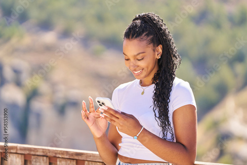 A woman with long hair is smiling while looking at her cell phone