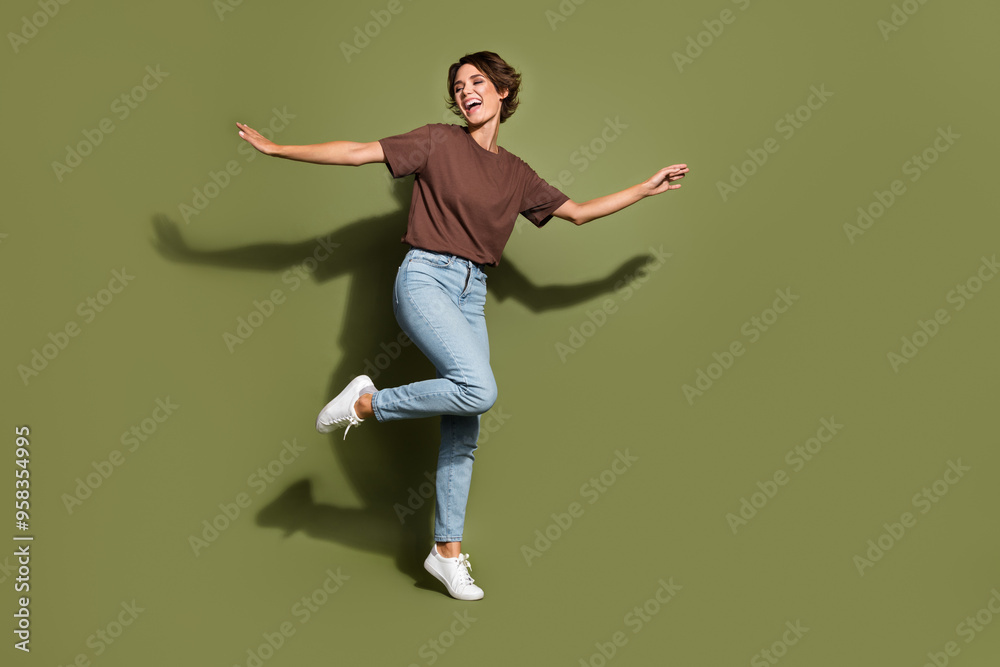 Full size photo of satisfied good mood woman dressed brown t-shirt jeans trousers dancing at party isolated on khaki color background Full size photo of satisfied good mood woman dressed brown t-shirt jeans trousers dancing at party isolated on khaki color background