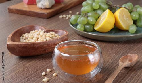 Fresh honey pour into glass bowl. Pine nuts in heart shaped plate. Wooden dishes and food on table. Useful natural food. 