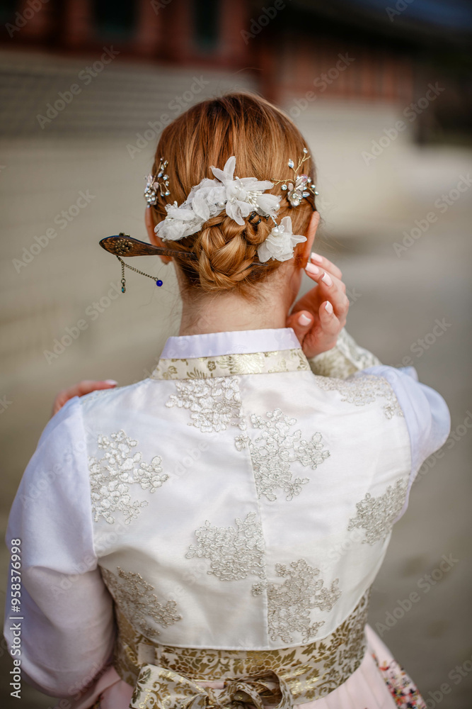 Picture of traditional Korean hairstyle for festive occasions. A girl dressed in a classic ethnic dress standing outdoor, view from the back.