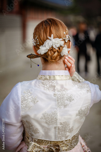 Picture of traditional Korean hairstyle for festive occasions. A girl dressed in a classic ethnic dress standing outdoor, view from the back.