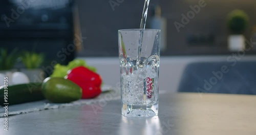 Close up transparent glass standing on the table top near vegetables and is filled with fresh water on the contemporary kitchen background