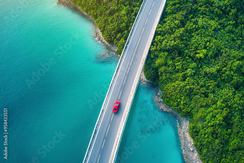 Aerial view of bridge road with red car over blue water lake or sea with island and green woods.