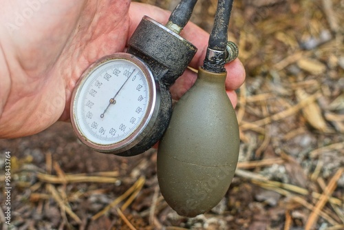  round modern with black arrows medical for measuring blood pressure white plastic tonometer together with a rubber gray bulb in hand near ground on the street photo