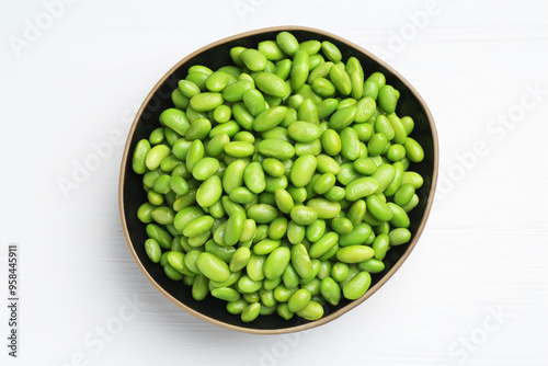 Fresh edamame soybeans in bowl on white wooden table, top view