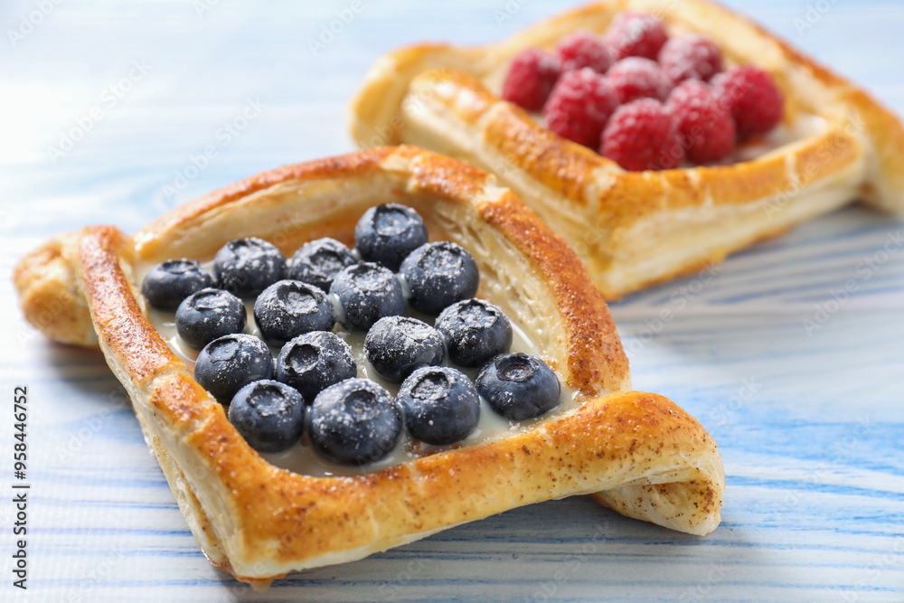 Tasty puff pastries with berries on light blue wooden table, closeup Tasty puff pastries with berries on light blue wooden table, closeup